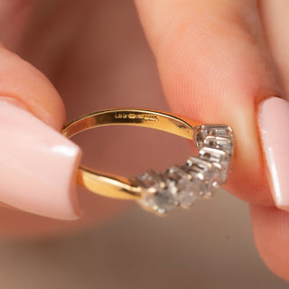 Gold ring with six diamonds held between fingers against a neutral background